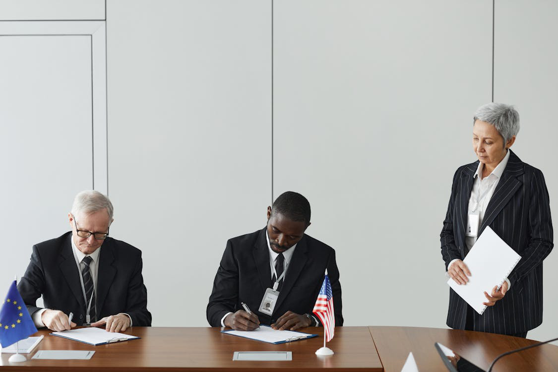 A woman standing beside two men signing documents